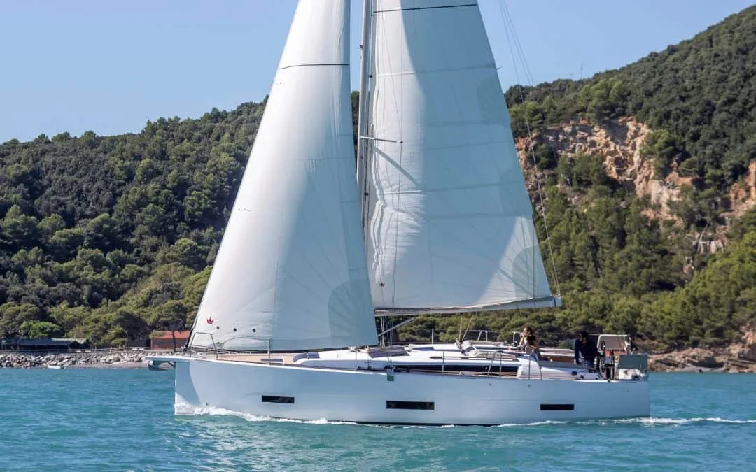 Ein Segelboot vom Typ Dufour 390 segelt im Wasser in der Nähe eines Berges.